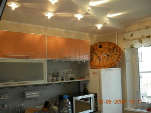 Готовая кухня по оканчании ремонта с комбинированны освещением подвесного потолка из ГКЛ, установленной кухонной мебелью, бытовой техникой, шторами на окне
